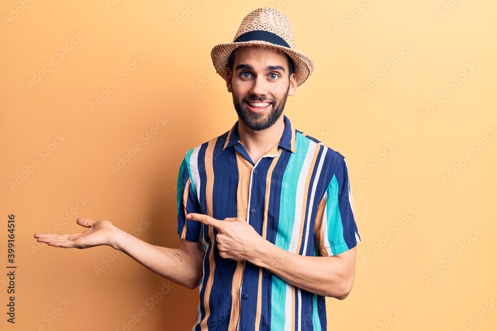 Young handsome man with beard wearing summer hat and shirt amazed and smiling to the camera while presenting with hand and pointing with finger. Young handsome man with beard wearing summer hat and shirt amazed and smiling to the camera while presenting with hand and pointing with finger.