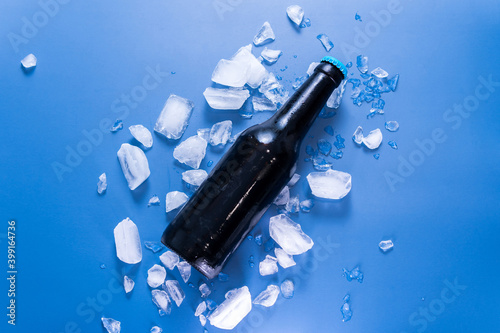 Bottle of beer with ice on blue background