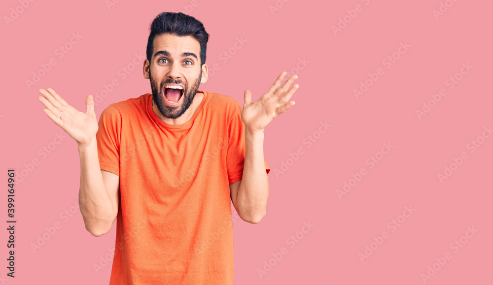 Young handsome man with beard wearing casual t-shirt celebrating crazy and amazed for success with arms raised and open eyes screaming excited. winner concept Young handsome man with beard wearing casual t-shirt celebrating crazy and amazed for success with arms raised and open eyes screaming excited. winner concept