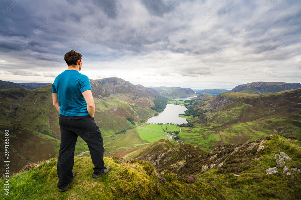 Naklejka premium Man standing on top of Haystacks peak looking at Buttermere lake in Lake District. England