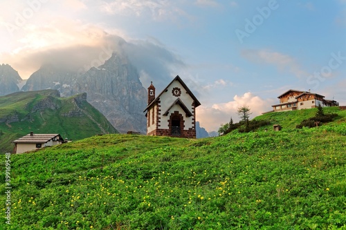 Summer scenery of Dolomites with view of a lovely church at the foothills of rugged mountain peaks ( Cimon della Pala ) under dramatic dawning sky in Passo Rolle, Dolomiti, South Tyrol, Italy, Europe