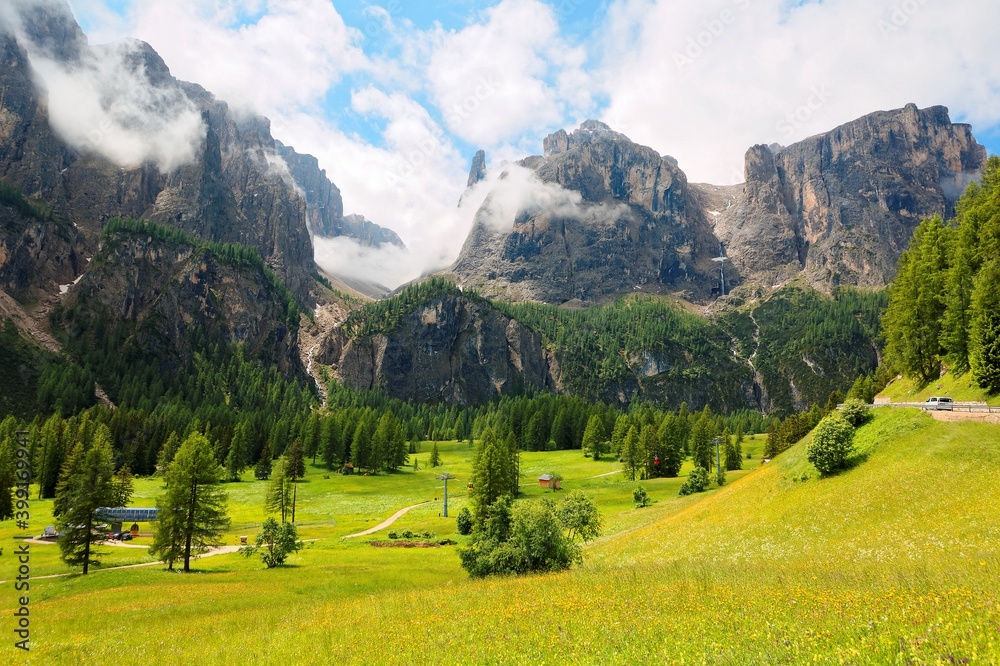 Summer scenery of majestic Sella mountains with waterfalls tumbling down rocky cliffs into a beautiful green grassy valley ~ Magnificent landscape of Dolomites in Pass Gardena, South Tyrol, Italy