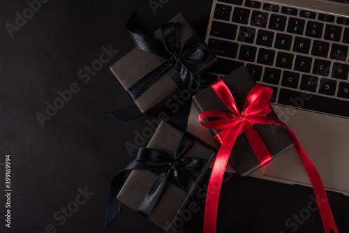 Black Friday sale online shopping commerce, Top view of gift box wrapped black paper and red bow ribbon present on a laptop computer keyboard, studio shot on black background