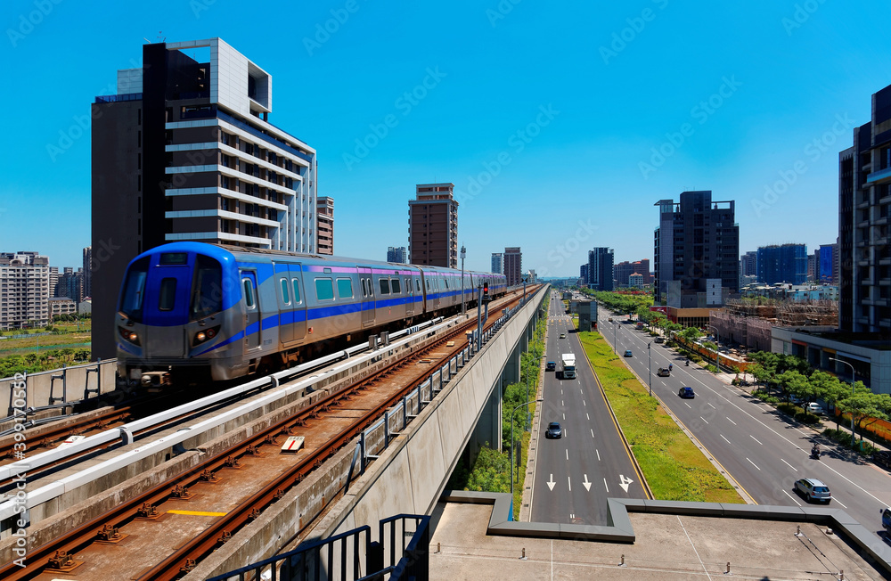 Scenic view of a metro train traveling on the elevated rails of Taoyuan Mass Rapid Transit System by residential towers under blue sunny sky in Chunli, Taoyuan, Taiwan 