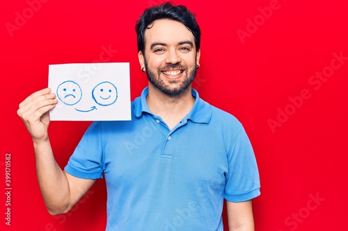 Young hispanic man holding sad to happy emotion paper looking positive and happy standing and smiling with a confident smile showing teeth © Krakenimages.com