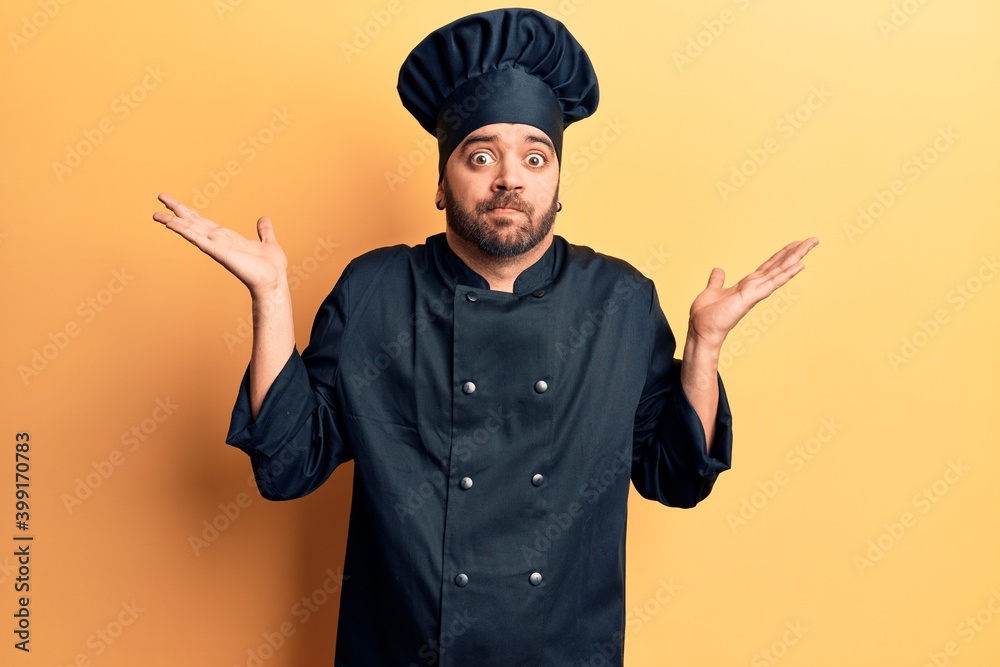 Young hispanic man wearing cooker uniform clueless and confused with open arms, no idea and doubtful face. Young hispanic man wearing cooker uniform clueless and confused with open arms, no idea and doubtful face.