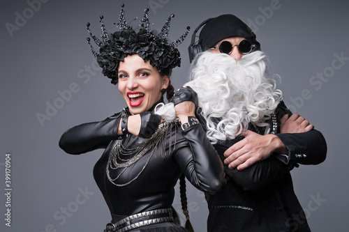 Dj Santa Claus with Sunglasses and Headphones Listening to Christmas Music and Snow Maiden Black Leather Jacket Having Fun. Rock Party Time. Studio Shot Over Grey Background.