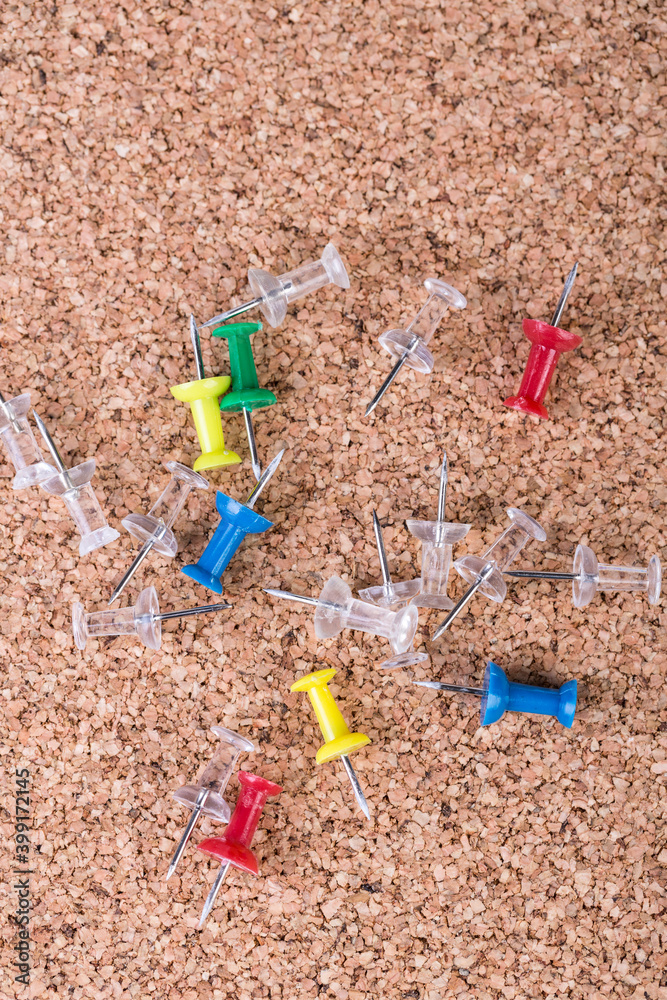 Scattered pile of multicolored thumb tacks on a brown cork board Scattered pile of multicolored thumb tacks on a brown cork board