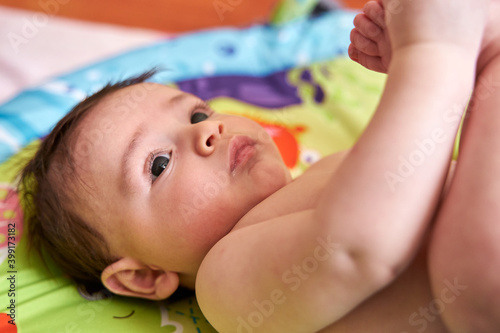 semi-nude caucasian newborn baby, with diapers lying on his back on the bed facing upwards playing with his feet, seen from above