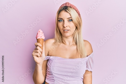 Young caucasian woman holding ice cream in shock face, looking skeptical and sarcastic, surprised with open mouth