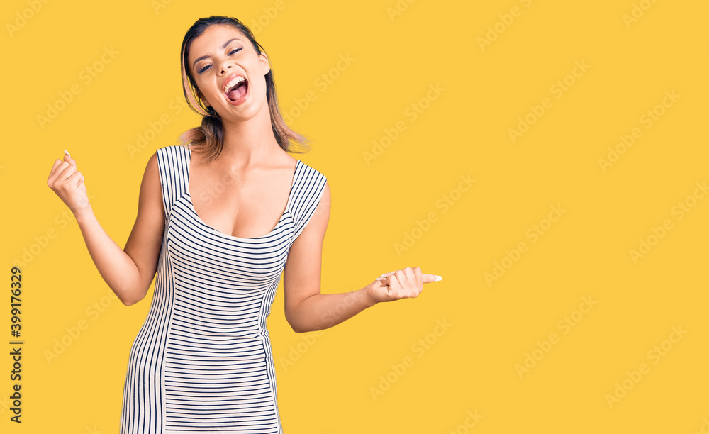 Young beautiful woman wearing casual dress screaming proud, celebrating victory and success very excited with raised arms Young beautiful woman wearing casual dress screaming proud, celebrating victory and success very excited with raised arms