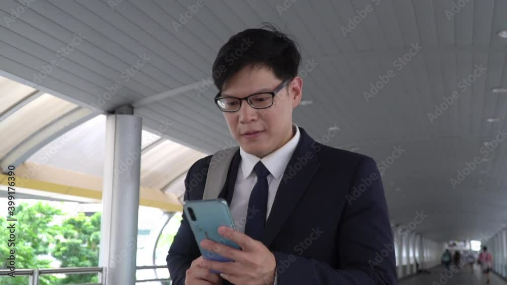 Confident Asian business man office worker in suit walking in city with texting online message on smartphone. Businessman using mobile phone for online working corporate business in office district Confident Asian business man office worker in suit walking in city with texting online message on smartphone. Businessman using mobile phone for online working corporate business in office district