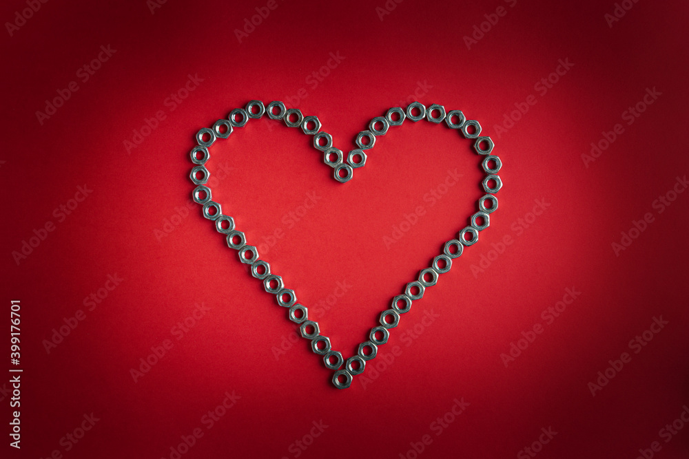 Heart made of metal nuts on a bright red background. Valentine's day symbol