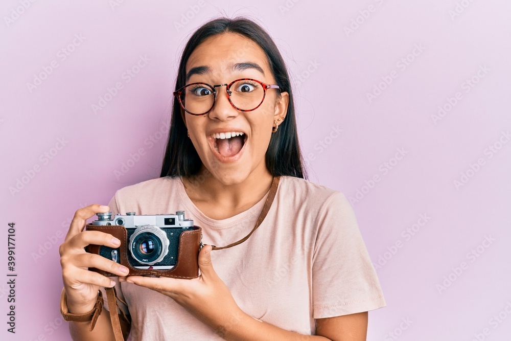 Young asian woman holding vintage camera celebrating crazy and amazed for success with open eyes screaming excited.