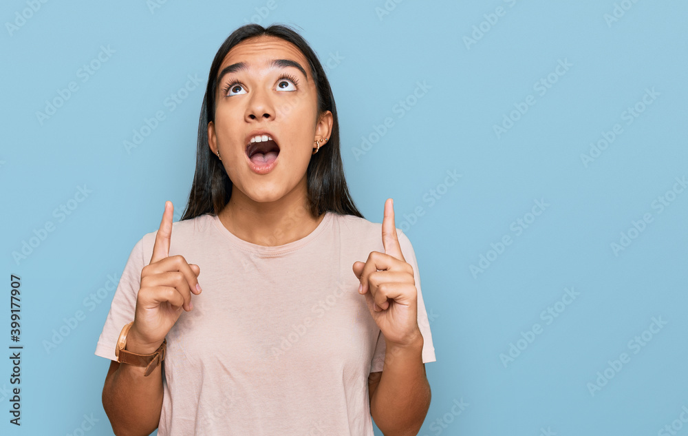Young asian woman wearing casual clothes amazed and surprised looking up and pointing with fingers and raised arms. Young asian woman wearing casual clothes amazed and surprised looking up and pointing with fingers and raised arms.