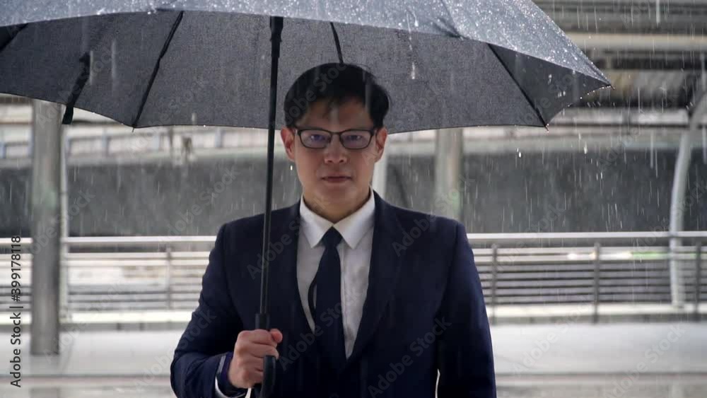 Portrait of Confidence Asian businessman office worker in suit holding black umbrella standing in the rain. Handsome man business people working in city office district in bad weather raining day. Portrait of Confidence Asian businessman office worker in suit holding black umbrella standing in the rain. Handsome man business people working in city office district in bad weather raining day.