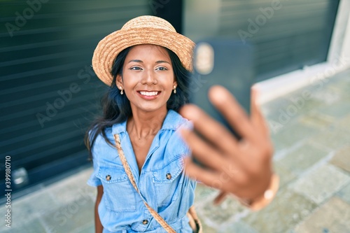 Young beautiful indian woman wearing summer hat smiling happy making selfie by the smartphone at the city. © Krakenimages.com