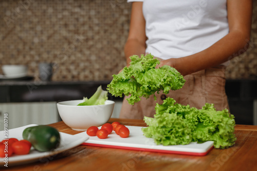 Cropped image unrecognisable woman cooking healthy food at home kitchen - lettuce salad, cherry tomatoes and cucumber