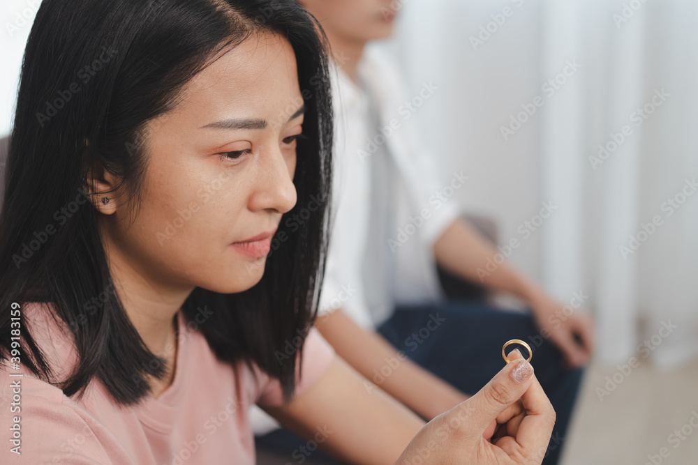 Unhappy young asian couples quarrel on the couch, relationships are in trouble. The wife holding the wedding ring in disappointment and upset for her husband, which may lead to divorce.
