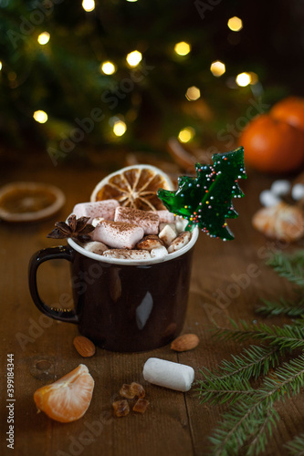 Christmas winter cocoa with marshmallow and lollipop in the shape of a Christmas tree in a brown cup on a wooden background. Vertical photo. Selective focus.