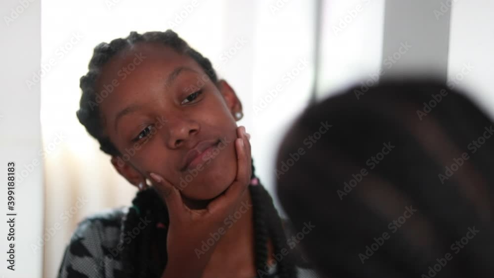 Teen black African girl inspecting her face in front of mirror Teen black African girl inspecting her face in front of mirror