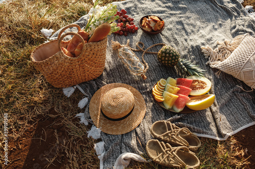 Beautiful summer picnic on the beach at sunset in boho style. Organic fresh fruit on linen blanket. Picnic background with basket, fruits and wicker bag with baguette