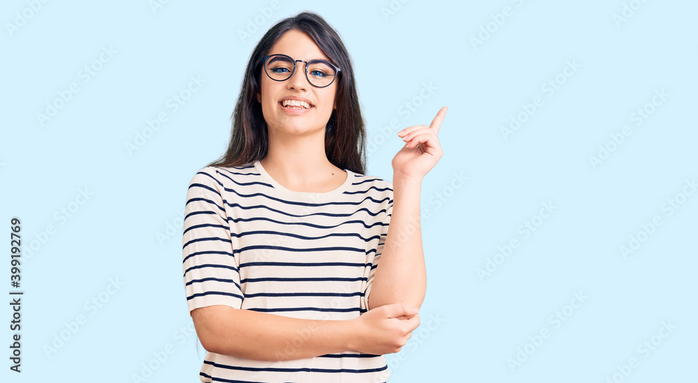 Brunette teenager girl wearing casual clothes and glasses with a big smile on face, pointing with hand and finger to the side looking at the camera. Brunette teenager girl wearing casual clothes and glasses with a big smile on face, pointing with hand and finger to the side looking at the camera.