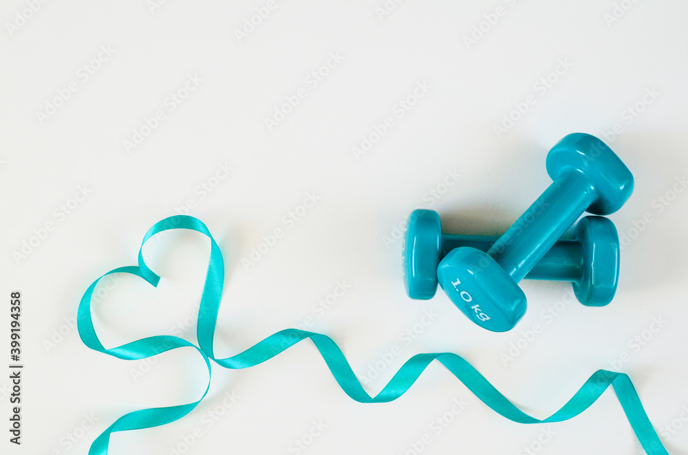 Two turquoise dumbbells with heart from ribbon on white background with copy space. Concept of Valentines day, love, healthy lifestyle, giving gifts, love of sports. Trendy color green tide. Two turquoise dumbbells with heart from ribbon on white background with copy space. Concept of Valentines day, love, healthy lifestyle, giving gifts, love of sports. Trendy color green tide.