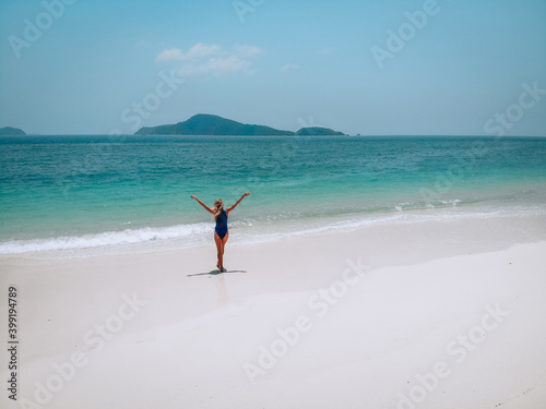 Young attractive woman in a blue swimming suit standing on a sandy beach and sunbathing. Summer vacation concept