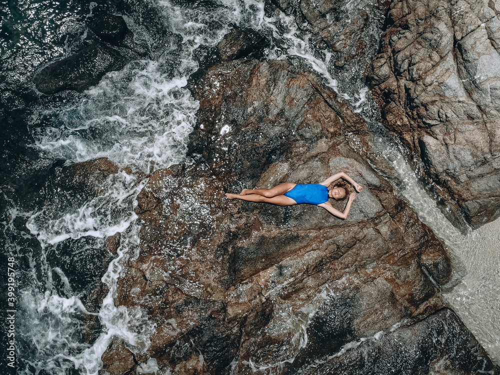 From above photo of a pretty young woman in a blue swimming suit lying on the rock in high tide. Summer vacation concept From above photo of a pretty young woman in a blue swimming suit lying on the rock in high tide. Summer vacation concept