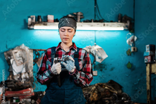 Portrait of a young female mechanic in uniform and gloves, holding a tool. Close-up of the employee's hands. Indoors © _KUBE_