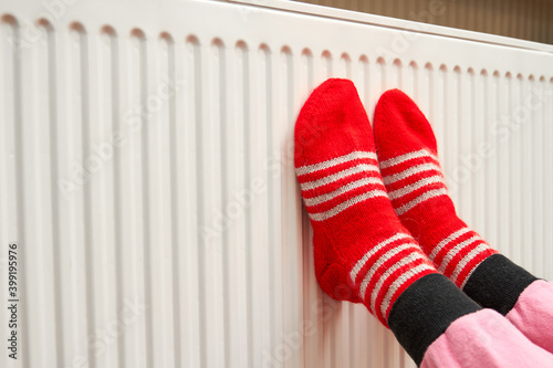 A girl in red woolen socks warms her feet on the radiator