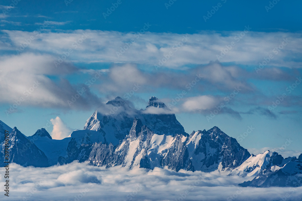 Beautiful panorama of high rocky mountains Ushba with mighty glaciers against the blue sky and clouds Beautiful panorama of high rocky mountains Ushba with mighty glaciers against the blue sky and clouds