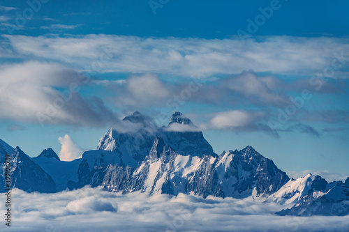 Beautiful panorama of high rocky mountains Ushba with mighty glaciers against the blue sky and clouds