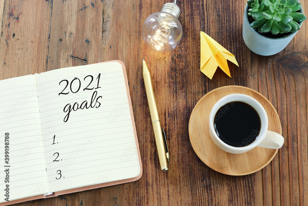 Business concept of top view 2021 goals list with notebook, cup of coffee over wooden desk Business concept of top view 2021 goals list with notebook, cup of coffee over wooden desk