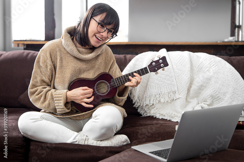 Young beautiful woman learning to play ukulele at home with online lessons. photo