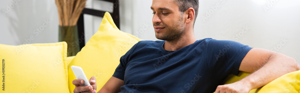 Fototapeta premium man using smartphone on couch at home, banner