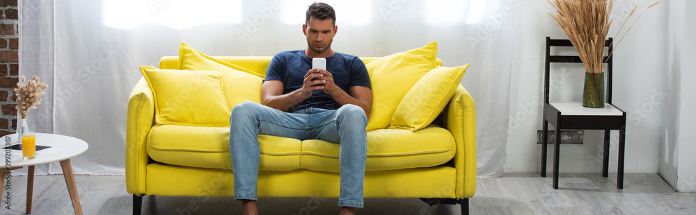 man sitting on couch while using smartphone near glass of orange juice on coffee table, banner man sitting on couch while using smartphone near glass of orange juice on coffee table, banner