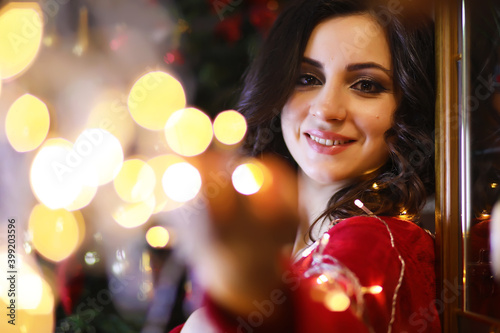Young attractive girl wearing warm pajamas and a bedspread near the New Year tree. Christmas atmosphere.