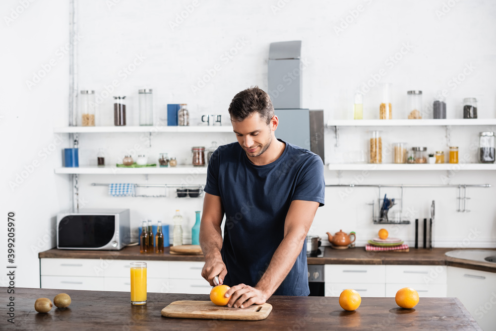  cutting orange on wooden cutting board near kiwi and glass o orange juice