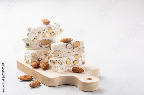 Torrone - soft italian nougat with almonds. On small wood board. White background. Copy space.