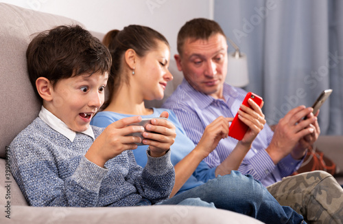 Modern young family absorbedly looking at smartphones in home interior .. photo