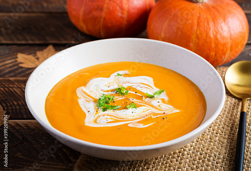 Pumpkin soup on rustic wooden table. Seasonal autumn food - Spicy pumpkin and carrot soup.