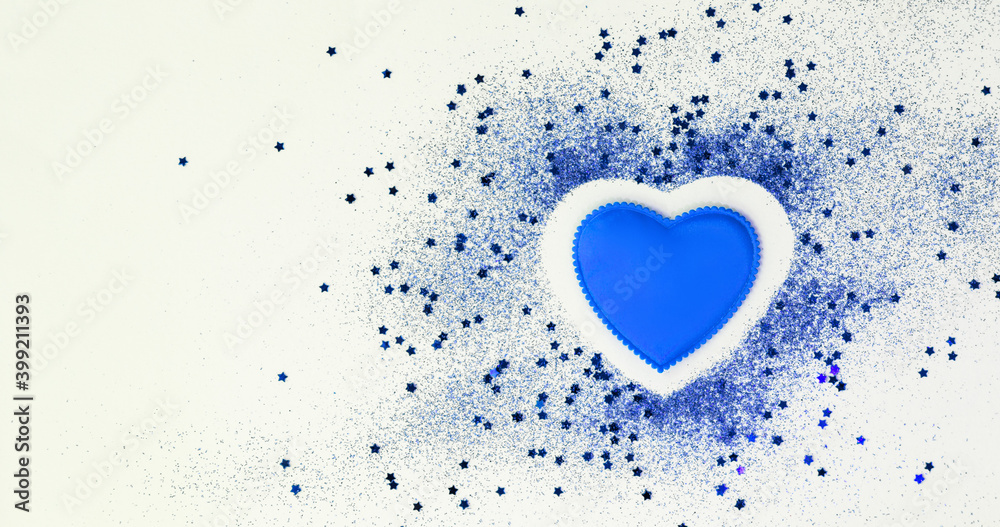 Blue confetti glitter in shape of heart on white festive background, copy space, valentines day festive card