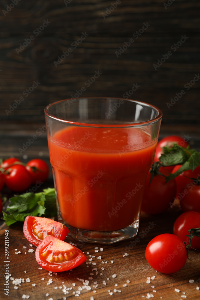 Glass of tomato juice, tomatoes and salt on wooden background