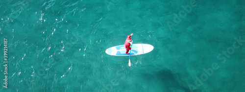 Photography Aerial drone ultra wide photo of Santa Claus paddle surfing in Caribbean turquoi