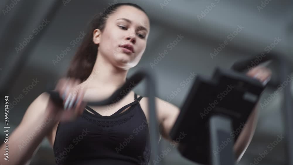 Young woman trains on a elliptical bike simulator, aerobic exercise and endurance training, low angle view.