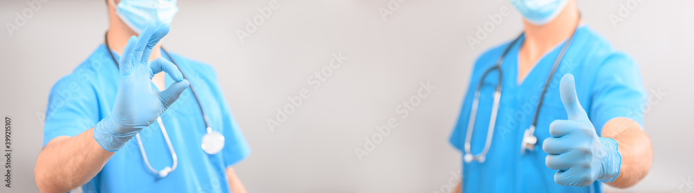 Two doctors or medical staff in blue uniforms and medical gloves on a gray background stand opposite each other show a thumbs up or like and OK Two doctors or medical staff in blue uniforms and medical gloves on a gray background stand opposite each other show a thumbs up or like and OK