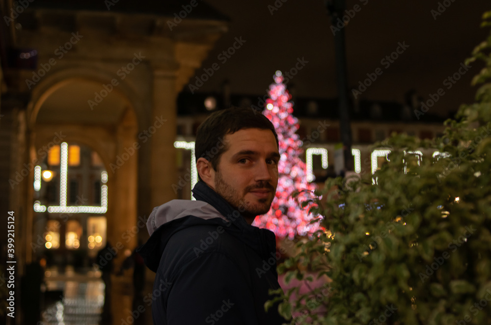 Photo of a young and attractive man smiling next to a Christmas tree at night full of beautiful lights. Christmas decorations. ornaments