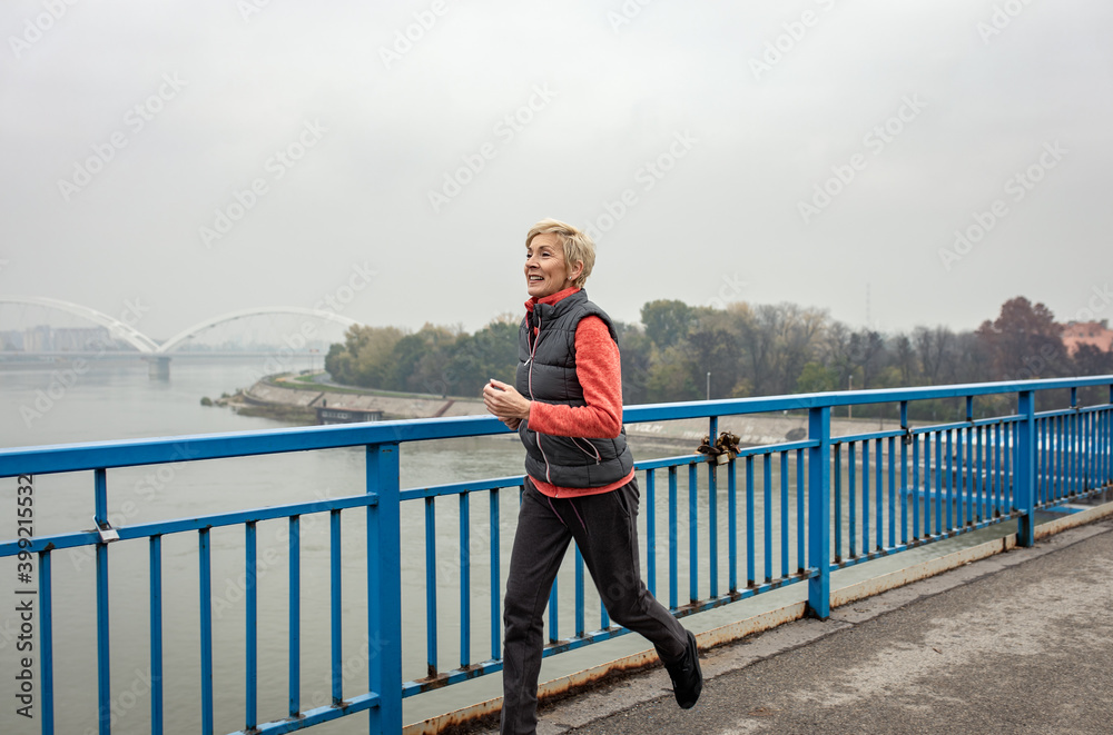 Active senior woman running through the city during the day. Active senior woman running through the city during the day.